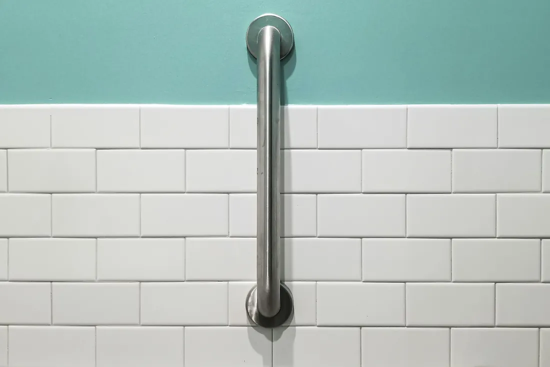 Barre d'appui verticale en inox fixée sur une faïence blanche de type métro, sous un mur peint vert d'eau (Lapeyrouse-Mornay, Drôme)