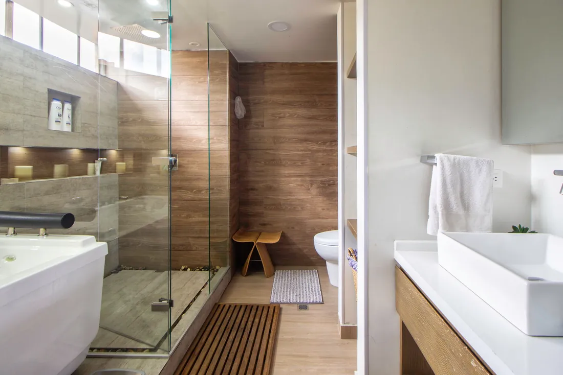 Grande douche vitrée de plain-pied en carrelage effet bois, avec un tabouret en bois à l'intérieur et un caillebotis devant l'entrée, baignoire au premier plan (Biganos, Gironde)