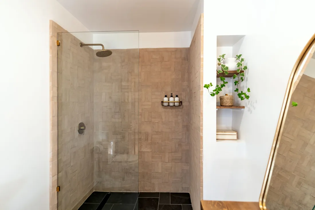 Douche à l'italienne fermée par une simple paroi vitrée, carrelage zellige rosé, sol en ardoise sombre avec caniveau, plantes dans une niche à côté (Montmorot, Jura)